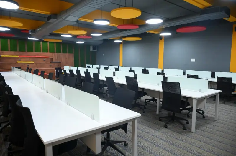 Open-plan student workspace with rows of desks and colourful ceiling lighting